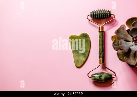 Jade Face Massagegeräte auf einem rosa Hintergrund neben einer saftigen. Stockfoto