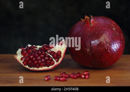 Ganzer roter Granatapfel und ein frisches Segment mit saftigen Samen auf einem Holztisch, dunkler Hintergrund. Granatapfel auf Holz auf dunklem Hintergrund Stockfoto