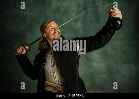 Porträt eines lächelnden Mannes, medeival Piraten hält Flasche Rum isoliert auf dunklem Hintergrund. Stockfoto