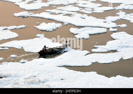 Non Exclusive: NEW DELHI, INDIEN - 9. NOVEMBER 2021: Ein Fischer reist in einem Boot und versucht, eine dicke Schicht giftigen Schaums zu überqueren, auf dem er schwimmt Stockfoto