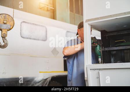 Ein Mann bohrt mit einem Bohrer ein Loch in die Rückseite eines Lastwagens. Stockfoto