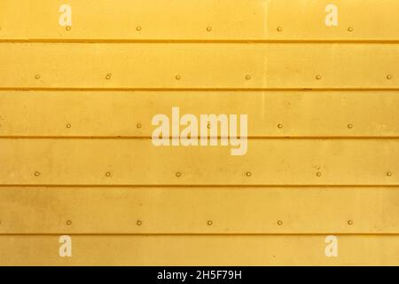 Hintergrund aus Wellblech in gelber Farbe. Die Textur der horizontalen Metallplatten, die von den Nieten verbunden sind. Leer für ein Poster oder Banner. Stockfoto