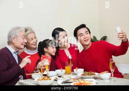 Fröhliche Familie, die beim Neujahrsessen zusammen Fotos macht Stockfoto