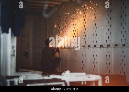 Ein Arbeiter in einem Eisenbehälter poliert Metall. Funken fliegen durch Reibung. Stockfoto