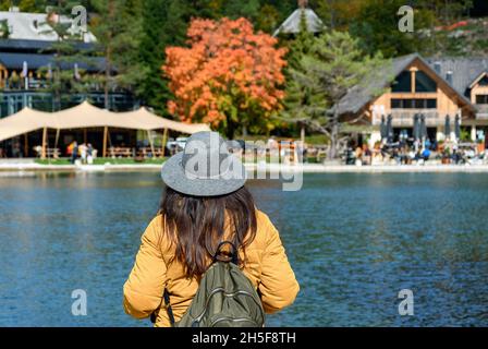 Rückansicht einer Frau, die am Ufer des Sees steht und auf ein wunderschönes Touristenresort blickt Stockfoto