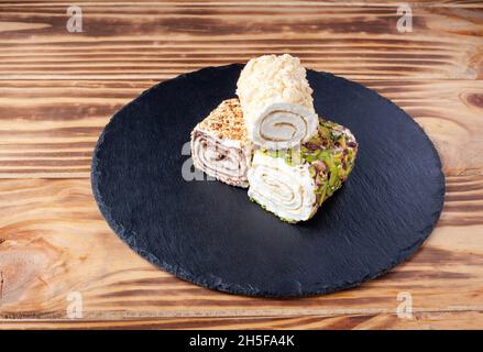 Türkisches Vergnügen. Auswahl an türkischen Köstlichkeiten mit verschiedenen Geschmacksrichtungen, die auf einem runden Steinteller cremig gefüllt sind. Lokum Rollen bedeckt Nüsse und Zuckerpulver. Stockfoto