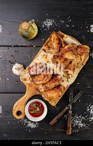 BBQ Hähnchen Oberschenkel und Flügel. Appetitlich gegrilltes Geflügelfleisch auf einem Holzschneidebrett. Dunkler rustikaler Hintergrund. Draufsicht. Vertikale Aufnahme Stockfoto