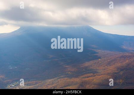 Blaue Berge Wolken Strahlen. Helles Sonnenlicht durch den Nebel erhellt die Gipfel. Atmosphärischer natürlicher Hintergrund-Kopierbereich. Ruhiger, neutralgrauer Herbst Stockfoto