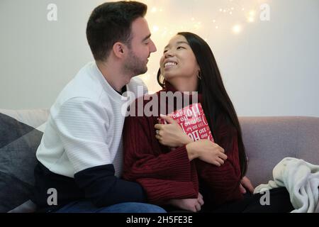 Romantisches junges multirassisches Paar, das Weihnachtsgeschenke austauscht. Stockfoto