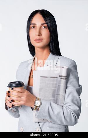 Geschäftsfrau mit einer Tasse Kaffee und einer Zeitung in einem modernen, hellen Anzug, der die goldene Uhr trägt und eine schwarze Maniküre hat. Stockfoto
