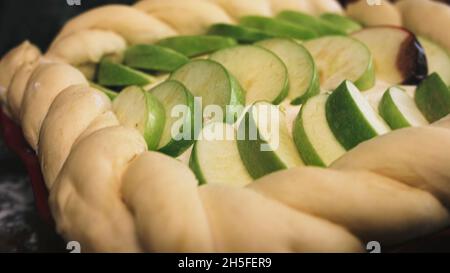 Nahaufnahme von rohem hausgemachtem Apfelkuchen vor dem Backen. Scheiben von frischen Äpfeln liegen in drei Reihen in rohem Teig, Konzept des Kochens und Lebensmittel. Stockfoto