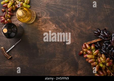 Weinflaschen mit Weintrauben und Weinläsern auf altem dunklen Holztischhintergrund mit Kopierraum. Rotwein mit Weinrebe. Weinkomposition auf rustikal Stockfoto