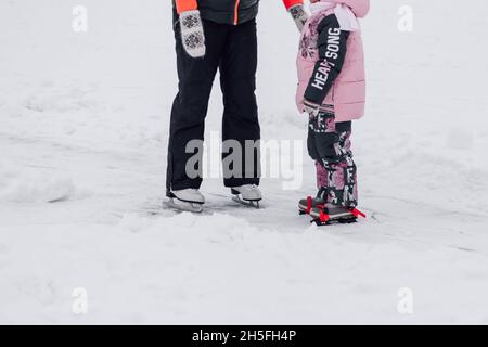 Nahaufnahme von menschlichen Beinen und Eiskunstlauf-Schlittschuhen. Junge Frau und kleines Mädchen Schlittschuh im Winter in der Natur auf Eis Stockfoto