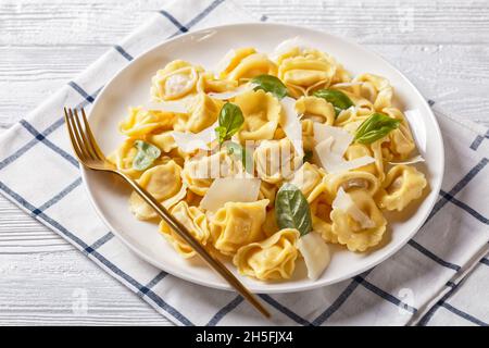 Tortelloni mit Käse- und Spinatfüllung, italienische Knödel auf einem weißen Teller auf einem weißen Holztisch, Nahaufnahme Stockfoto