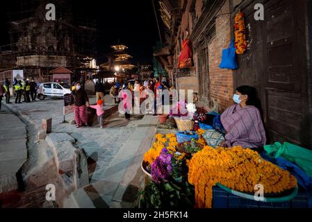 Lalitpur, Bagmati, Nepal. November 2021. Eine lokale Frau, die eine schützende Gesichtsmaske trägt, verkauft am Abend an der Ecke des Patan Durbar Square, einer UNESCO-Weltkulturerbestätte in Lalitpur, Nepal, am 9. November 2021 Blumen. (Bild: © Sunil Sharma/ZUMA Press Wire) Stockfoto