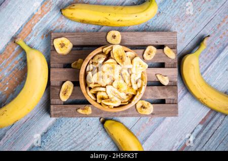 Draufsicht auf dehydrierte organische Bananenchips auf dem Holzbrett, verziert mit frischen Bananen Stockfoto