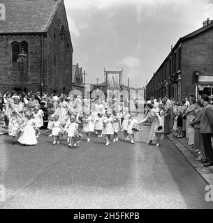 1950, historische, junge sonntagsschüler, die an einer Straßenprozession in Audley Range, Blackburn, Lancashire, England, Großbritannien, teilnehmen, Eine lange Straße viktorianischer Reihenhäuser im Norden Englands. Hinter den Kindern wird eine handgesäte Decke oder ein Banner auf Stangen für die Audley Range Congregatonal Church hochgehalten. Stockfoto