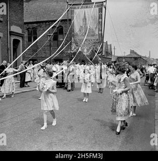 In den 1950er Jahren nahmen historische, sonntags Schulkinder an einer Straßenprozession Teil und hielten Rippons, die an Holzpfosten befestigt waren, und stützten eine große, von Hand gesäte Decke für die Audley Range Congrational Church, Audley Range, Blackburn, Lancashire, England, VEREINIGTES KÖNIGREICH. Seit den 1840er Jahren hatten die industrielle Revolution und das Wachstum der Baumwolle- und Textilindustrie viele Gebiete im Norden Englands verändert und Reihenhäuser, Schulen, Geschäfte, Pubs und Kirchen wurden auf Ackerland gebaut, um die neue Bevölkerung zu nutzen, die in den Fabriken und Textilfabriken arbeitete. Stockfoto