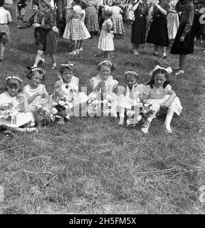 In den 1950er Jahren, historische junge Mädchen in ihren sonntagsschulkleidung und mit Blumensträußen, die sich auf dem Rasen in einem lokalen Park niedersetzten, nachdem sie mit ihren Familien an einer Straßenprozession für die Audley Range Congregational Church, Audley Range, Blackburn, Lancashire, England, teilgenommen hatten, VEREINIGTES KÖNIGREICH. Ab den 1840er Jahren hatten die industrielle Revolution und das Wachstum der Baumwolle- und Textilindustrie das Gebiet verändert und Reihenhäuser, Schulen, Geschäfte, Pubs und Kirchen wurden auf Ackerland gebaut, um die neue Bevölkerung zu nutzen, die in den Fabriken und Textilfabriken arbeitet. Stockfoto