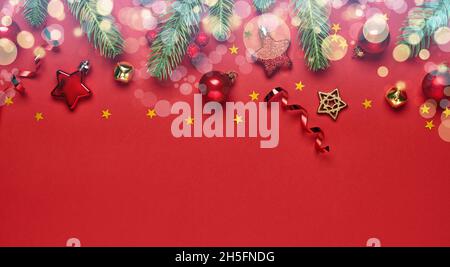 Weihnachtsbanner. Tannenzweige und Weihnachtsdekorationen auf rotem Hintergrund mit Bokeh. Draufsicht. Stockfoto