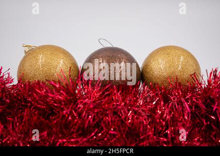 Linie aus zwei goldenen und einer braunen Weihnachtskugeln mit rotem Lametta vorne isoliert auf weißem Hintergrund. Stockfoto
