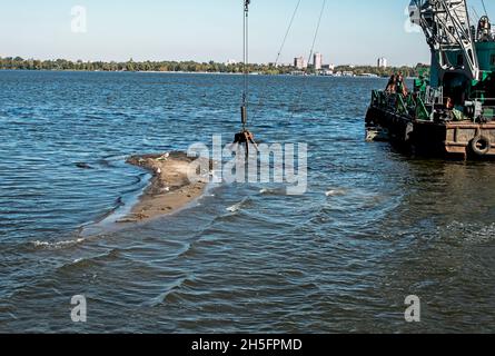 Reinigung der neu entstandenen Insel von Industrieabfällen am Dnjepr River durch einen Bagger. Umweltprobleme moderner Flüsse. Ökologisches Konzept. Stockfoto