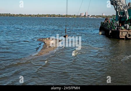 Reinigung der neu entstandenen Insel von Industrieabfällen am Dnjepr River durch einen Bagger. Umweltprobleme moderner Flüsse. Ökologisches Konzept. Stockfoto