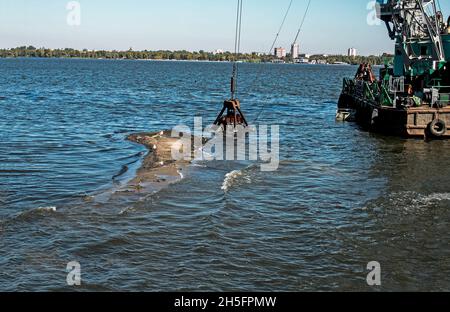 Reinigung der neu entstandenen Insel von Industrieabfällen am Dnjepr River durch einen Bagger. Umweltprobleme moderner Flüsse. Ökologisches Konzept. Stockfoto