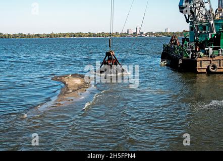 Reinigung der neu entstandenen Insel von Industrieabfällen am Dnjepr River durch einen Bagger. Umweltprobleme moderner Flüsse. Ökologisches Konzept. Stockfoto