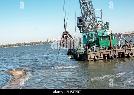 Reinigung der neu entstandenen Insel von Industrieabfällen am Dnjepr River durch einen Bagger. Umweltprobleme moderner Flüsse. Ökologisches Konzept. Stockfoto