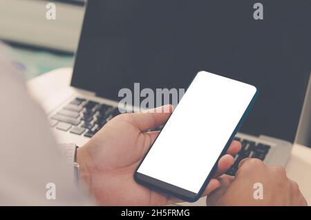 Mann mit einem Smartphone mit einem leeren Bildschirm für die Gestaltung oder Werbung mit einem Laptop-Computer. Beschneidungspfad Stockfoto
