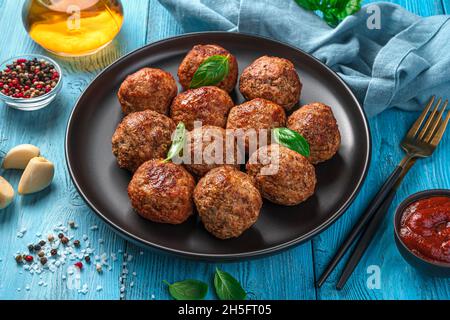Fleischbällchen mit frischem Basilikum auf blauem Hintergrund. Seitenansicht, Nahaufnahme. Stockfoto
