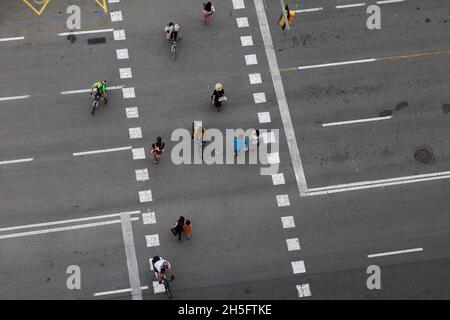 Fußgänger und Radfahrer (keine Erkennbarkeit) auf einer grauen Verkehrsstraße mit weißen gebohrten Linien. Keine Autos. Aus der Vogelperspektive. Stockfoto