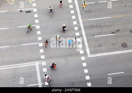 Fußgänger und Radfahrer (keine Erkennbarkeit) auf einer grauen Verkehrsstraße mit weißen gebohrten Linien. Keine Autos. Aus der Vogelperspektive. Stockfoto