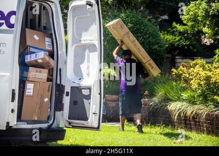 07-14-2020 Tulsa USA Delivery man trägt eine große Kiste über dem Kopf, wobei die Hintertür zum Lieferwagen offen ist und viele weitere Kisten in einer grünen Nachbarschaft zu sehen sind Stockfoto