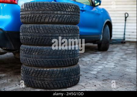 Satz von Winterreifen neben dem Auto im Radservice, das Konzept des saisonalen Reifenwechsels Stockfoto