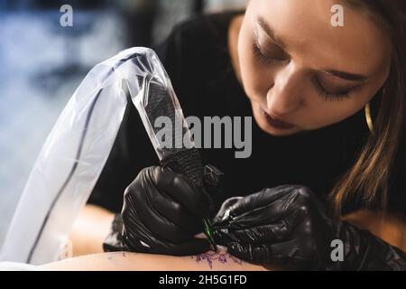 Nahaufnahme eines Tattoos auf dem Bein. Eine Tattoo-Künstlerin macht eine Zeichnung mit einer speziellen Maschine in einem Kunststudio Stockfoto