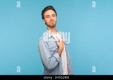 Porträt eines Mannes, der Denim-Hemd trägt, sich zeigt und mit arrogantem egoistischem Ausdruck aussieht, sich erfolgreich und selbstwichtig fühlt. Innenaufnahme des Studios isoliert auf blauem Hintergrund. Stockfoto