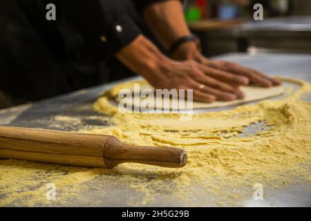 Der professionelle Koch kocht im Küchenrestaurant des Hotels und bereitet das Abendessen zu. Ein Koch in einer Schürze macht eine Pizza. Man rollt Pizzateig aus Stockfoto