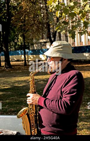 Dnepropetrovsk, Ukraine - 09.17.2021: Ein Mann spielt im Park Saxophon. Straßenmusiker mit Saxophon, der Musik für wohltätige Zwecke aufführt. Öffentlich solo Stockfoto