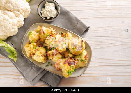 Blumenkohlblüten, gebraten mit Ei und Schinken auf einem grauen Teller, serviert mit Frischkäse-Dip auf einer Serviette und einem Holztisch, Kopierraum, Blick aus der Höhe Stockfoto