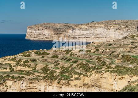 Felsige Kalksteinküste der Insel Gozo und Mittelmeer mit türkisblauem Wasser und Höhlen. Grüne terrassenförmige Felder, Hügel. Beliebte Wanderklippen Stockfoto