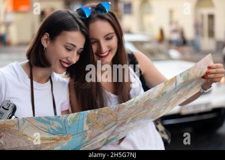 Zwei junge attraktive Mädchen ruhen sich in der Stadt aus, reisen in die Stadt, besichtigen, navigieren durch die Karte, fotografieren mit der Kamera, glücklich Stockfoto