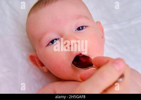 Die Mutter gibt das Medikament Säugling Baby in den Mund auf einem Löffel, orale Eisenlösung für niedrigen Hämglöm im Kind Stockfoto