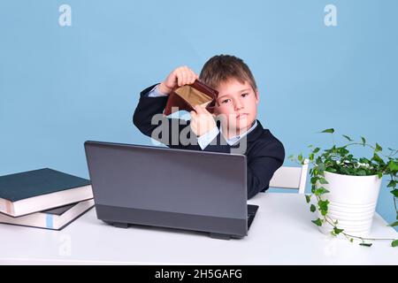 Ein Junge in einem Schulanzug mit einer leeren Brieftasche, kopieren Sie Platz auf einem blauen Studiohintergrund Stockfoto