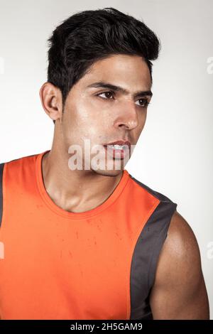 Porträt von müde hübsch Brünette sportlichen Mann trägt orange Sportkleidung Blick weg mit erschöpft Gesichtsausdruck, posiert nach dem Training. Innenaufnahme des Studios isoliert auf grauem Hintergrund. Stockfoto