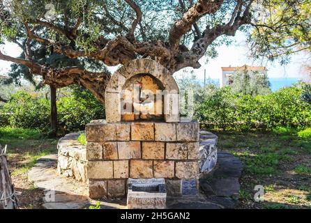 Brunnen im Dorfpark des kleinen Peloponnes Griechisches Dorf Kardamyli unter altem Olivenbaum mit Blick auf Villa im Hintergrund Stockfoto