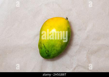 Reife grüne und gelbe Mangofrucht auf braunem Bastelpapier. Draufsicht. Stockfoto
