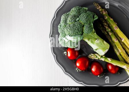 Gemüse auf dem Teller stehen auf dem Tisch, frische Kirschtomaten, Spargel und Brokkoli, Gemüsesalat, vegetarisches Mittagessen, Vegetarisches Abendessen, Speisen pro Stockfoto