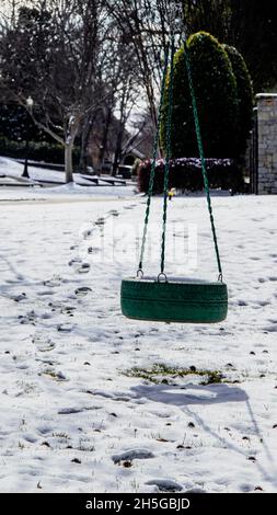 Grüner Reifen schwingen im Nachbarschaftshof im Schnee mit Schatten und Fußabdrücke, die vom Nachbarschaftshof zum Schwingen führen. Stockfoto